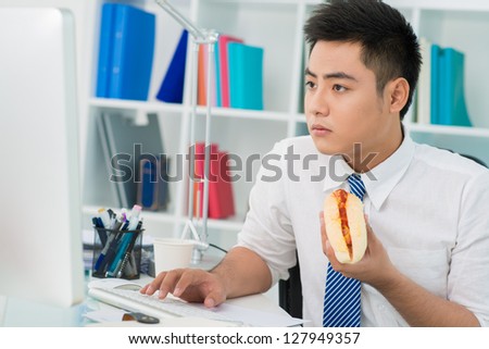 Busy office guy eating a hot-dog instead of a proper lunch