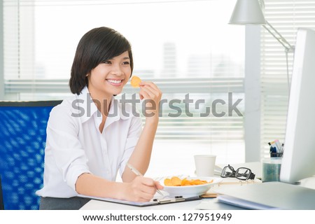 Young businesswoman doing paperwork and eating crisps