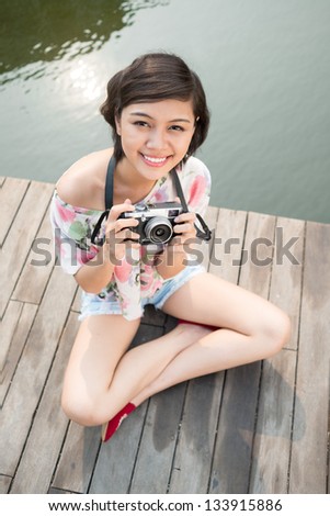 Young lady with a camera sitting on the bridge