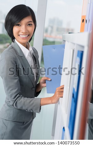 Vertical portrait of an attractive office worker with a folder on the foreground
