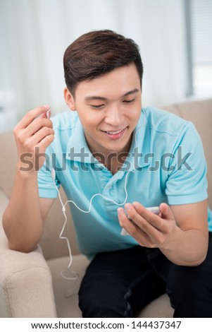 Vertical image of a smiling guy enjoying cool music on his smart phone