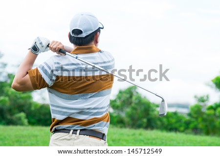 A golfer playing golf viewed behind outdoors