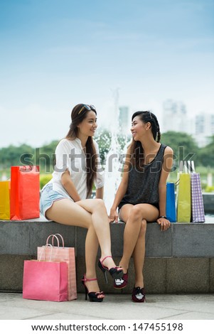 Vertical image of two lovely girlfriends talking after shopping on the waterworks outside