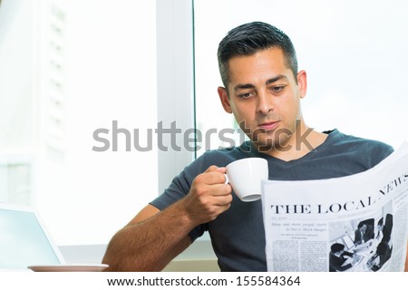 Copy-spaced image of a young man drinking morning coffee and reading the newspaper at home