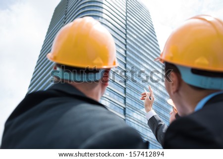 Back view of professional constructor workers discussing something while one of them pointing at something on the foreground