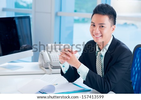 Close-up portrait of a financial broker at his workplace smiling and looking at camera on the foreground