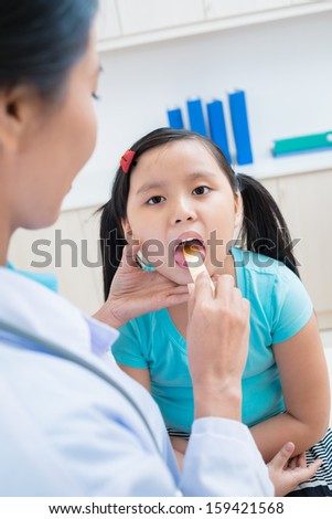 Vertical portrait of a little girl having throat\'??s examination on the foreground