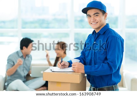 Portrait of a smiling delivery-boy writing in the application form and looking at camera on the foreground