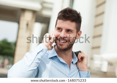 Close-up image of a young cheerful businessman talking by phone outside