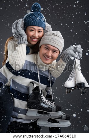 Vertical portrait of a young cheerful couple holding figure skates and having fun in winter weather