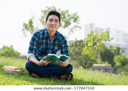 Image of a cheerful student sitting in lotus with books in the park