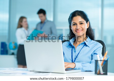 Closeup portrait of a young business lady typing and looking at camera on the foreground