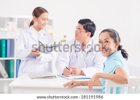 Close-up portrait of a senior patient looking at camera while doctor and nurse discussing on the foreground