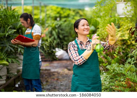 Happy Asian woman spraying water on plants in the greenhouse with mature man on background