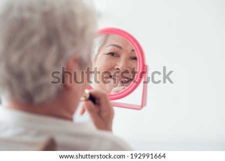 Pretty aged woman putting on lipstick, rear view