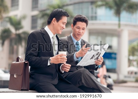 Two Asian businessmen discussing article in the newspaper