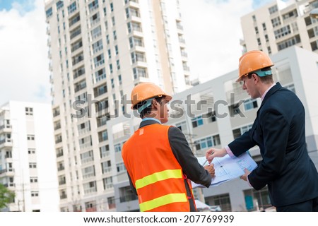 Architect and client discussing the plan of the building at the construction site, rear view
