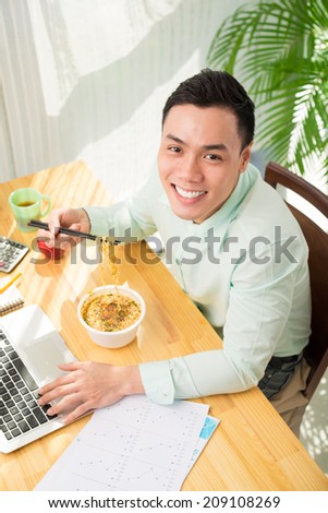 Happy Vietnamese businessman eating instant noodle soup for lunch