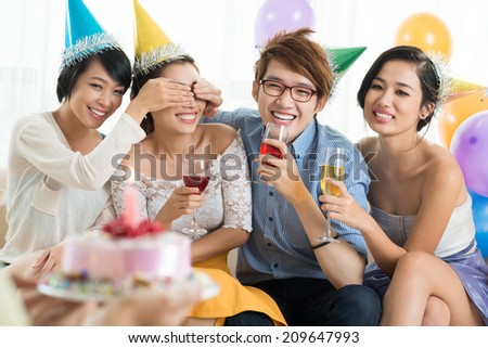 Young people covering eyes of their friend to give her a birthday cake
