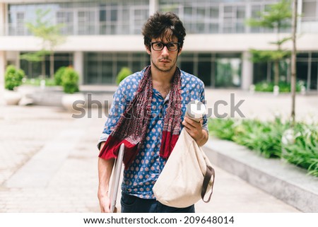 Pensive university student with bag and laptop walking on campus