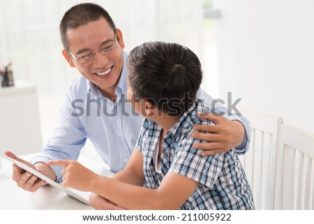 Asian father and son talking and using digital tablet
