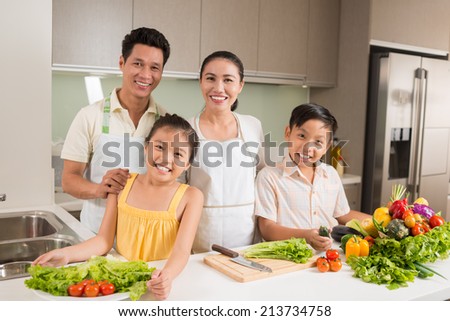 Portrait of smiling Asian family standing in the kitchen with vegetables on the table