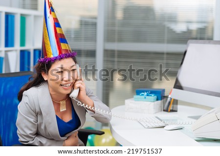 Businesswoman in a party hat talking on the phone at her desk