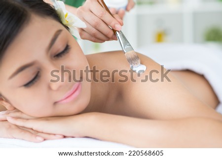 Hand of cosmetologist applying mask to the back of female patient