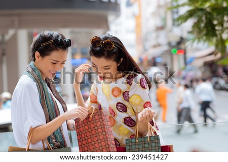 Asian girl showing something in the shopping bag to her friend