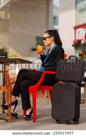 Stylish business lady with suitcases sitting in the cafe and drinking cocktail