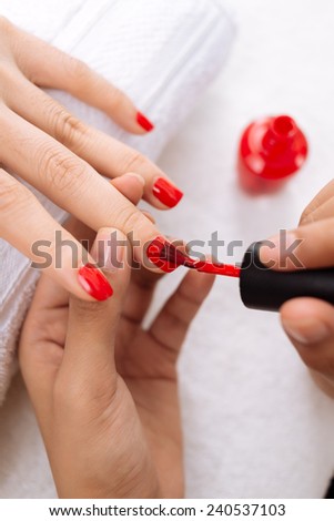 Master applying red nail polish to finger nails, selective focus