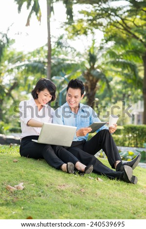 Pretty Asian business lady showing her colleague something on her laptop screen