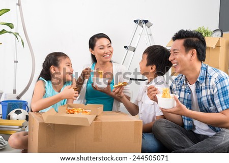 Vietnamese family sitting on the floor and eating noodles and pizza in their new house