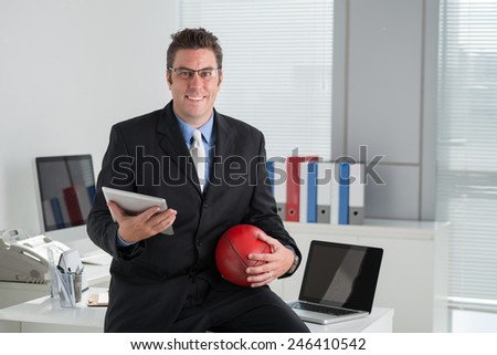 Happy middle-aged businessman with a football ball and digital tablet in the office