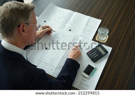 Mature engineer checking blueprint and making calculations