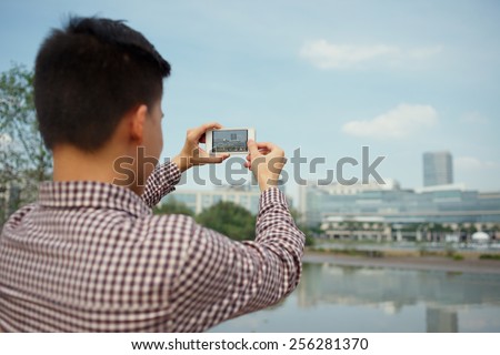 Young man taking picture of the cityscape with smartphone