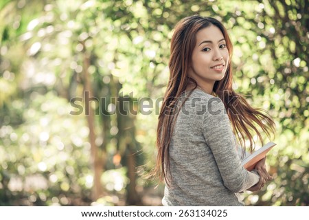 Portrait of attractive young Vietnamese woman reading in the park