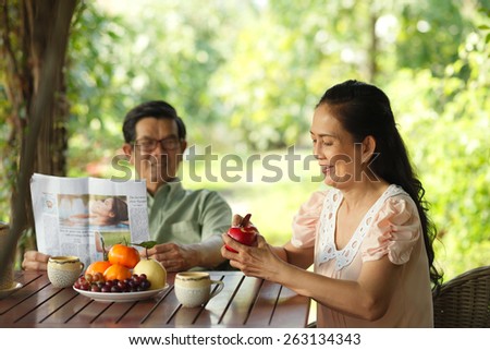 Aged family breakfast: woman peeling an apple while her husband reading a newspaper