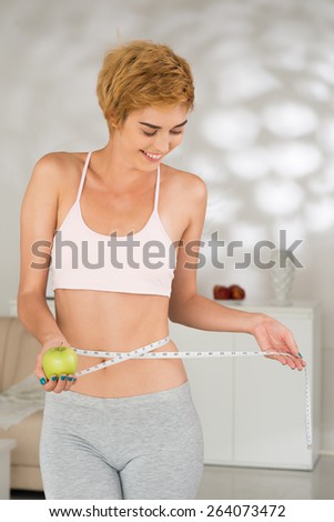 Sporty woman measuring waist and holding green apple: healthy eating and fitness concept