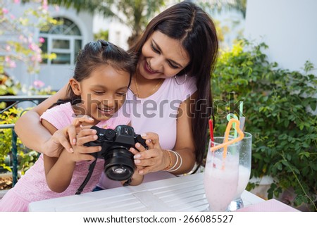 Smiling Indian mother and daughter looking at the photos on digital camera
