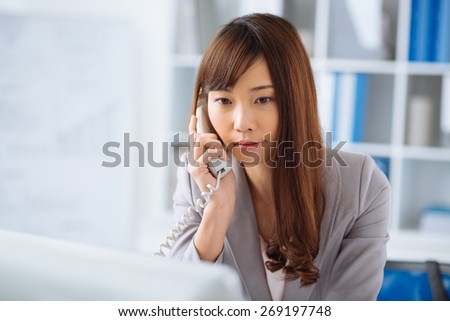 Female manager talking on the telephone while reading information on the computer screen