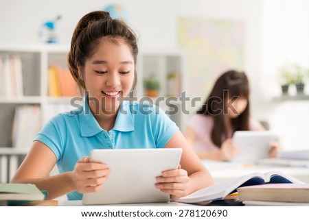 Smiling Asian schoolgirl using digital tablet in the class