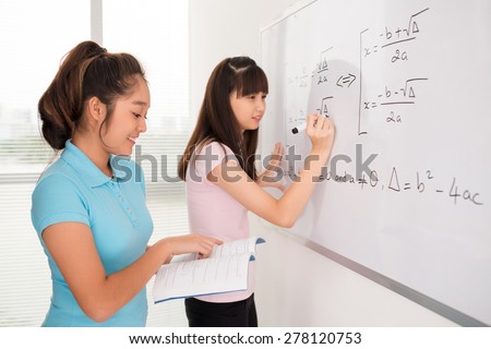 Asian schoolgirls writing equations from the manual of algebra on the whiteboard