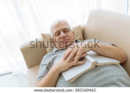 Senior man sleeping on sofa with a book