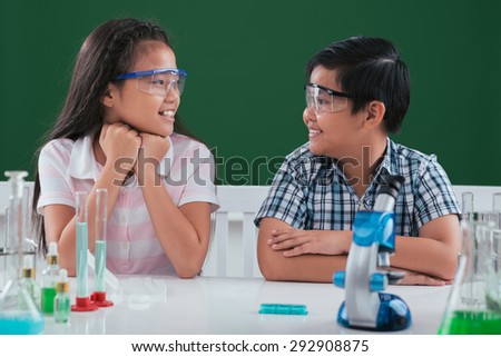 Asian boy and girl sitting at the desk in chemistry class and looking at each other