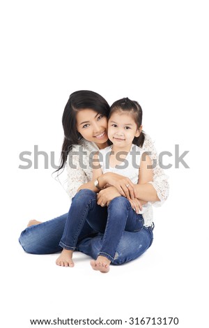 Studio portrait of Asian mother and daughter in jeans and white tops sitting on the floor