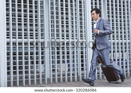 Vietnamese businessman with suitcase running late for flight