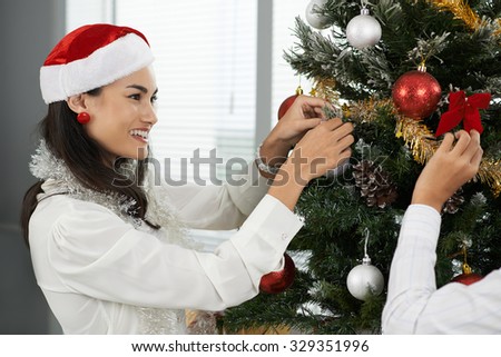 Pretty smiling business lady decorating Christmas tree in the office