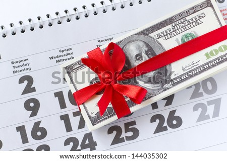 Money as a gift. Roll of money tied up by a red tape on a calendar