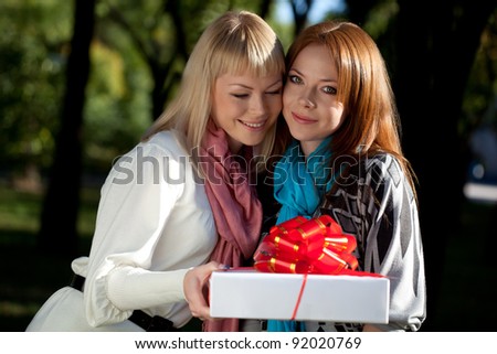 two happy sisters with gift in the summer park, one looking at camera